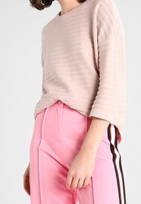 Hellrosa, gerippter Oberteil mit rundem Halsausschnitt und Dreiviertelärmeln, kombiniert mit rosa Hosen, die schwarze und weiße Seitenstreifen aufweisen.