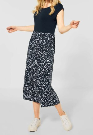 Marineblå kjole med tætsiddende overdel og udvidet hvid nederdel med polkaprikker, med korte ærmer og kombineret med hvide sneakers.