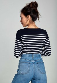 Marineblauw en witte gestreepte blouse met lange mouwen, gecombineerd met high-waisted blauwe jeans, met achterzakken en een getailleerde pasvorm.