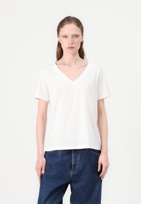 White short-sleeve V-neck t-shirt with a relaxed fit and smooth texture, paired with dark blue loose-fitting jeans.