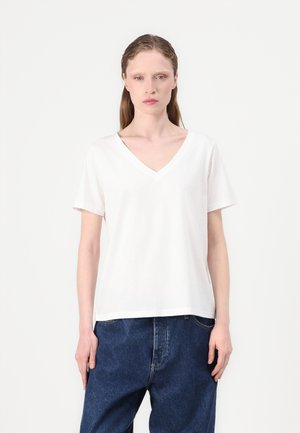 Weißes T-Shirt mit kurzem Ärmel und V-Ausschnitt in lockerem Schnitt und glatter Textur, kombiniert mit dunkelblauen, weit geschnittenen Jeans.