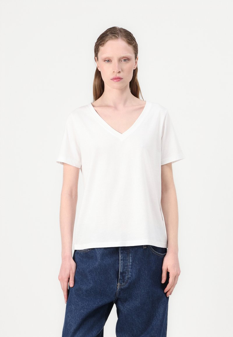 White short-sleeve V-neck t-shirt with a relaxed fit and smooth texture, paired with dark blue loose-fitting jeans.