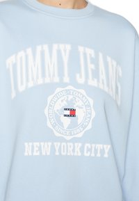 Felpa azzurra con il testo bianco "TOMMY JEANS", un logo a globo e la scritta "NEW YORK CITY" stampata sotto.