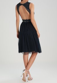 Svart klänning med en rygglös design, dekorerad liv, och en tyllkjol. Silverfärgade högklackade skor kompletterar outfiten.