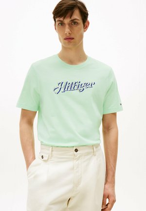Mørkegrøn bomulds T-shirt med "Hilfiger" broderet i blå. Korte ærmer, rund hals, båret med cremefarvede bukser.