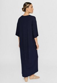 Marineblaues geripptes Midikleid mit weiten Ärmeln, rundem Ausschnitt und lockerer Passform, kombiniert mit hellbeigen gewebten Slippern.