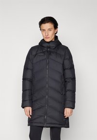 Svart isolerad pufferjacka med en chevronmönster, dragkedjestängning, huva och sidofickor. Materialet verkar slätt och lätt.