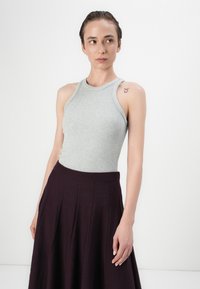 Haut sans manches en maille gris avec un col montant, associé à une jupe plissée violet foncé avec une large ceinture.