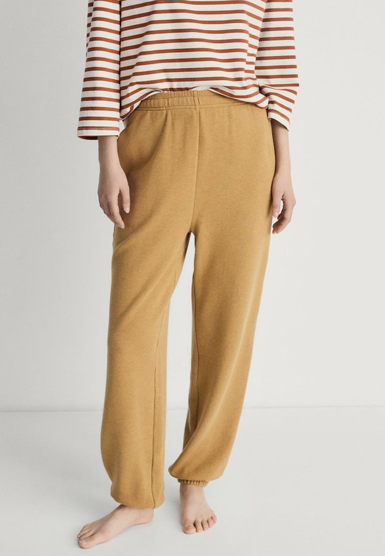 Mosterdkleurige sweatpants met een elastische tailleband, taps toelopende manchetten en een zachte, fleecachtige textuur. Draagt een gestreepte langemouwenshirt.
