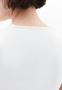 Top bianco in tessuto a coste con scollatura rotonda. Cuciture lungo il collo e una texture liscia, visto da dietro.