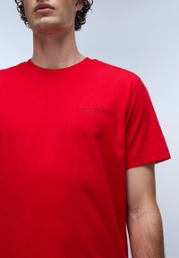 T-shirt in cotone rosso con scollo rotondo e maniche corte. Logo ricamato "NAPAPIJRI geographic" in rosso scuro sul petto.