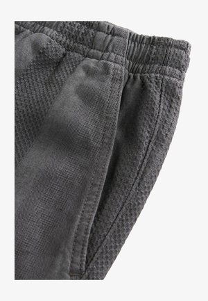 Shorts de sport gris en tissu texturé, avec une taille élastique côtelée et des poches latérales, montrés sous un angle pour mettre en valeur les détails.