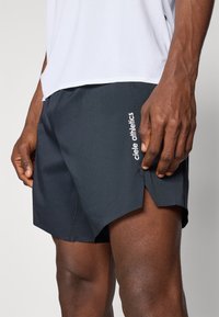 Black athletic shorts with a lightweight fabric, side slits, and a white logo "ciele athletics" on the left leg. Close-up of the fit.