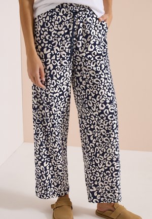 Marineblauwe broek met witte luipaardprint, elastische tailleband met trekkoord, gedragen met beige instapschoenen en een witte top.
