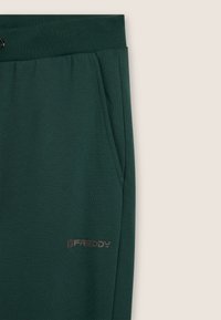 Pantalones de chándal verde oscuro con bolsillo lateral y cinturilla elástica, presentando un pequeño logo "FREDDY" cerca del bolsillo.