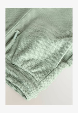 Svetlozelena teksturirana tkanina s herringbone vzorcem, z elastičnim pasom in manšetami za prilagajanje in udobje.