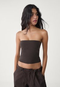 Hnědý crop top bez ramínek ze strečového materiálu, těsně přiléhající střih s hladkou texturou, kombinovaný s tmavými kalhotami s vysokým pasem.