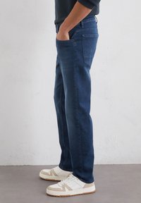 Jeans blu scuro con una vestibilità a gamba dritta, tasche laterali e un design semplice. Abbinati a sneakers bianche e beige.