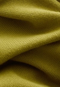 Tela de punto suave de color verde oliva con textura visible y pliegues suaves que crean sombras y profundidad.