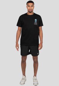 Camiseta de algodón negra con un logo gráfico azul en el pecho, combinada con pantalones cortos negros y zapatillas grises. Diseño simple y cómodo.