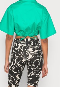 Chemisier turquoise court à manches courtes avec un dos froncé. Short de cycliste à motif marbré noir et crème avec une coupe ajustée.