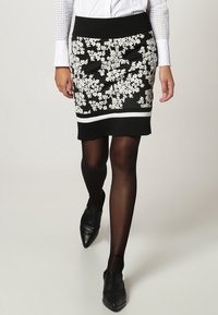 Czarna spódnica ołówkowa z białym haftem kwiatowym, solidną czarną talią i białym paskiem na dole. Gładki materiał i dopasowany fason.