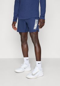 Námornícke modré športové šortky s logom "YANKEES" v bielej farbe, spárované s bielymi teniskami Nike a pruhovanými ponožkami. Materiál vyzerá ľahký a priedušný.
