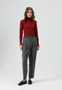 Rode coltrui met lange mouwen en knoopaccenten, gecombineerd met grijze geplooide broek en zwarte loafers. Eenvoudig, op maat gemaakt ontwerp.