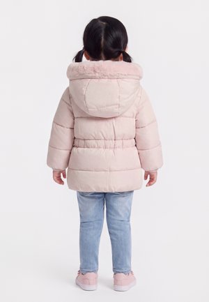Bambino con capelli scuri a codini che indossa una giacca imbottita rosa chiaro con cappuccio, jeans blu e scarpe da ginnastica rosa, in piedi di spalle.