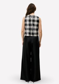 Zwart-wit geruit mouwloos top met een ronde hals en textuurstof, gecombineerd met zwarte, hooggetailleerde, wijde broekspijpen.