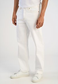 Pantalones vaqueros blancos de denim con costuras amarillas, diseño de pierna recta y estilo de cinco bolsillos, combinados con zapatillas bajas blancas.