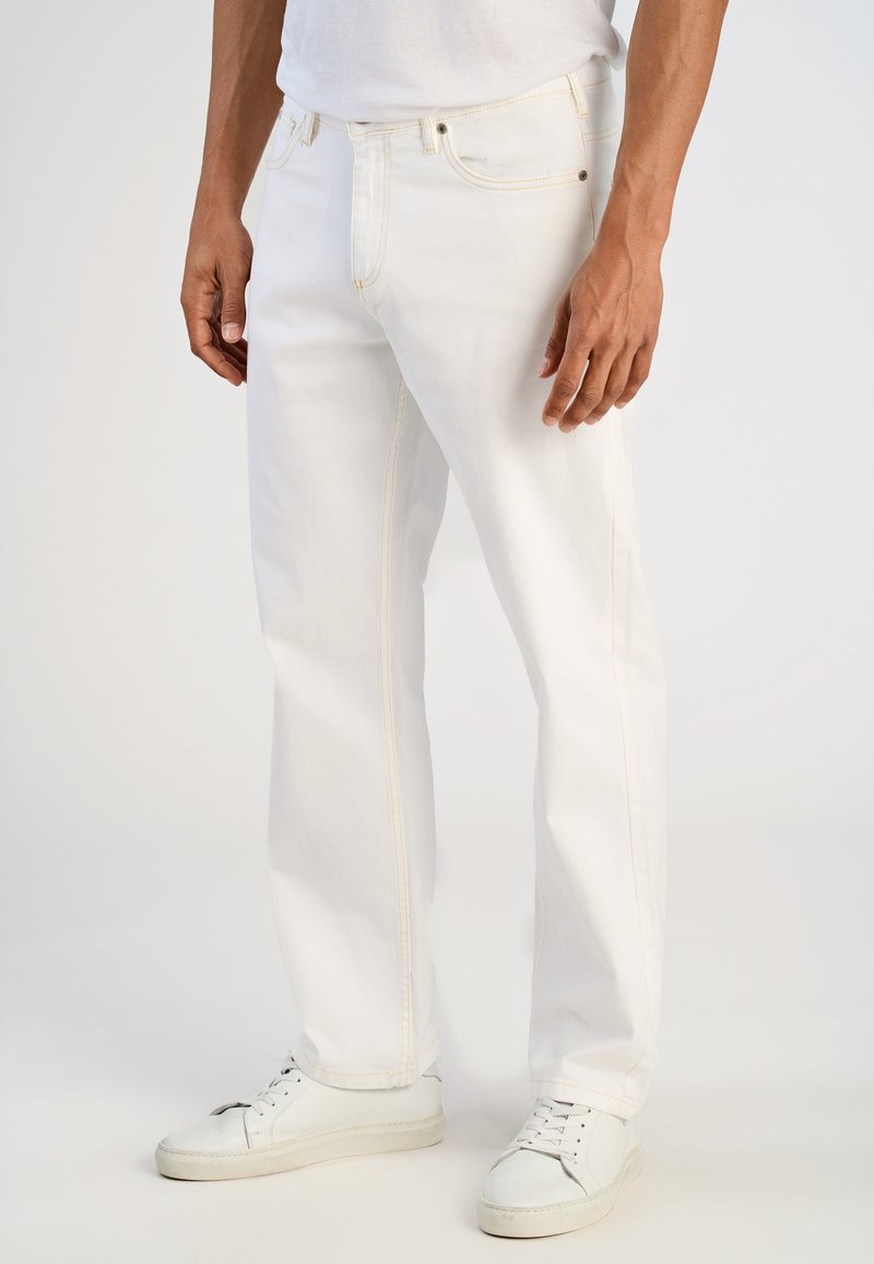 Pantalones vaqueros blancos de denim con costuras amarillas, diseño de pierna recta y estilo de cinco bolsillos, combinados con zapatillas bajas blancas.