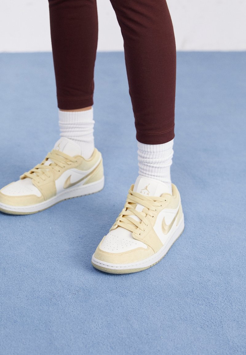 Baskets Nike Air en blanc et jaune, avec une empeigne en cuir lisse, une languette en mesh, des lacets ronds et une semelle texturée. Portées avec des chaussettes blanches.