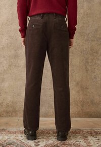 Braune Cord-Hosen mit geradem Bein, ausgestattet mit zwei Gesäßtaschen und schwarzen Knöpfen, kombiniert mit einem dunkelroten Pullover.