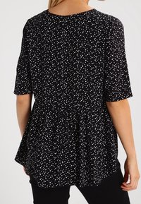 Blusa nera con maniche corte, caratterizzata da un orlo peplum e una stampa a forma di cuore bianca su tutta la superficie. Tessuto morbido con una vestibilità comoda.