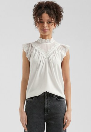 Blusa bianca con dettagli in pizzo e maniche a volant, caratterizzata da un colletto alto e una scollatura arricciata. Tessuto morbido e leggero.