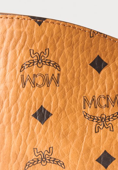 Gros plan de cuir texturé couleur fauve avec le logo MCM noir et des motifs en forme de losanges imprimés sur la surface.
