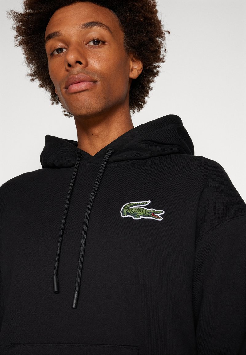 Felpa nera in cotone con tasca a marsupio, cappuccio con coulisse e logo di coccodrillo ricamato verde sul lato sinistro del petto.