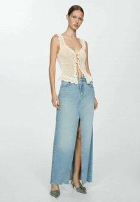 Top in maglia crema con bordi arricciati e scollatura lace-up, abbinato a una gonna maxi in denim blu chiaro con spacco davanti e orlo sfilacciato.