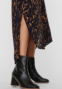 Piernas que llevan una falda de estampado animal negro y marrón con una gran abertura y botas de cuero negro hasta el tobillo con tacones anchos.