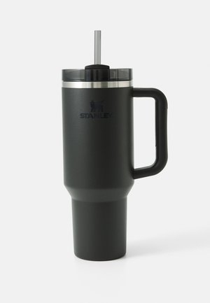 Caneca de viagem em aço inoxidável preto com forma cónica, um grande pega e uma tampa transparente com um canudo de metal. Logo "STANLEY" visível.