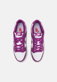 Sapatilhas Nike com base branca e detalhes em roxo, bico arredondado, detalhes perfurados e atacadores planos. Logotipo vermelho na língua.