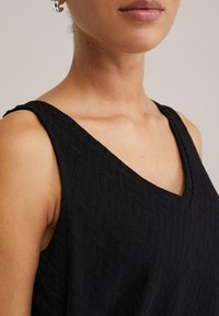 Top senza maniche nero con scollatura a V, caratterizzato da un motivo testurizzato di diamanti intrecciati. Tessuto liscio con una leggera lucentezza.