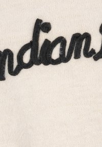 Krämfärgad stickad tyg med framträdande svart broderad text. Texturen verkar mjuk och något lurvig med en subtil glans.