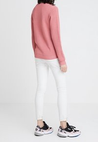 Maglione a maglia di un delicato rosa, jeans skinny bianchi e scarpe da ginnastica nere/rosa. La texture del maglione è a nido d'ape; i jeans sono attillati.