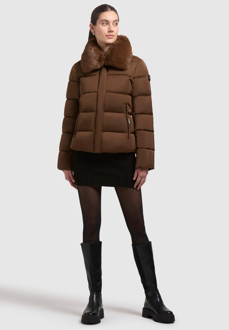 Brun pufferjakke med krave af kunstpels, lynlåslommer, quiltet design, parret med en sort ribbet miniskirt og knæhøje sorte støvler.