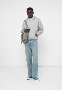 Siv hoodie z sprednjim žepom, svetlo modri naravnost krojeni jeans, in zeleni ter beli tenisiki. Siva torba čez ramo z detajlom sprednjega žepa.