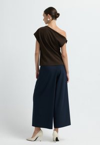 Top marrone asimmetrico con maniche corte abbinato a pantaloni larghi blu navy e tacchi alti beige. Tessuto morbido con una vestibilità rilassata.