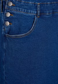 Denim suknja s tamnoplavim pranjem, prednjim zatvaranjem na pet dugmadi sa srebrnim dodacima i klasičnim dizajnom džepova. Glatka tekstura.