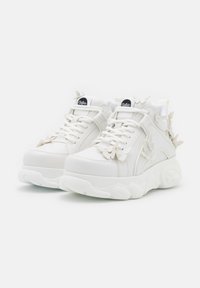 Baskets à plateforme blanches avec des décorations papillons sur les lacets et les côtés, dotées de semelles épaisses et du logo de la marque Buffalo sur la languette.